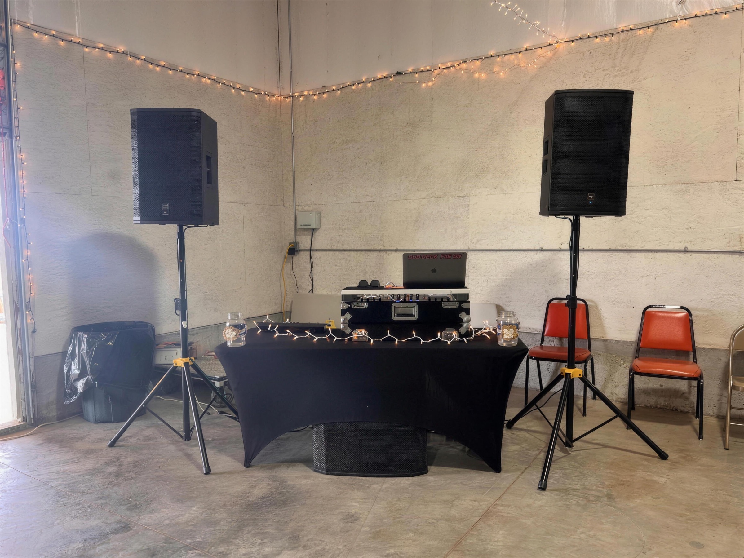 DJ table and two speakers on stands set up in an empty white hall